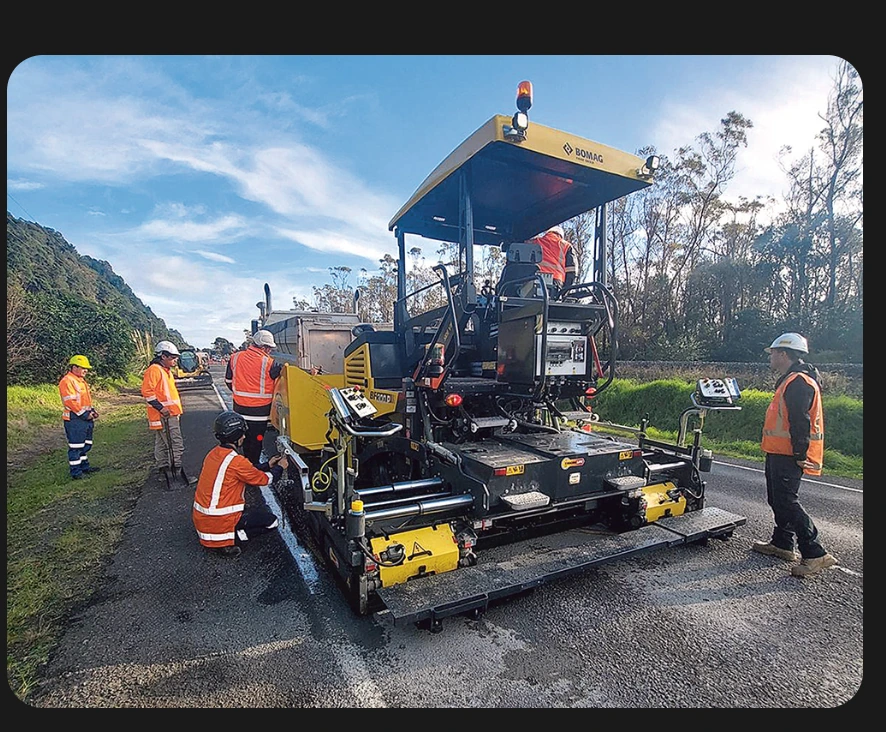 Crew around a yellow BOMAG asphalt paver on a rural road